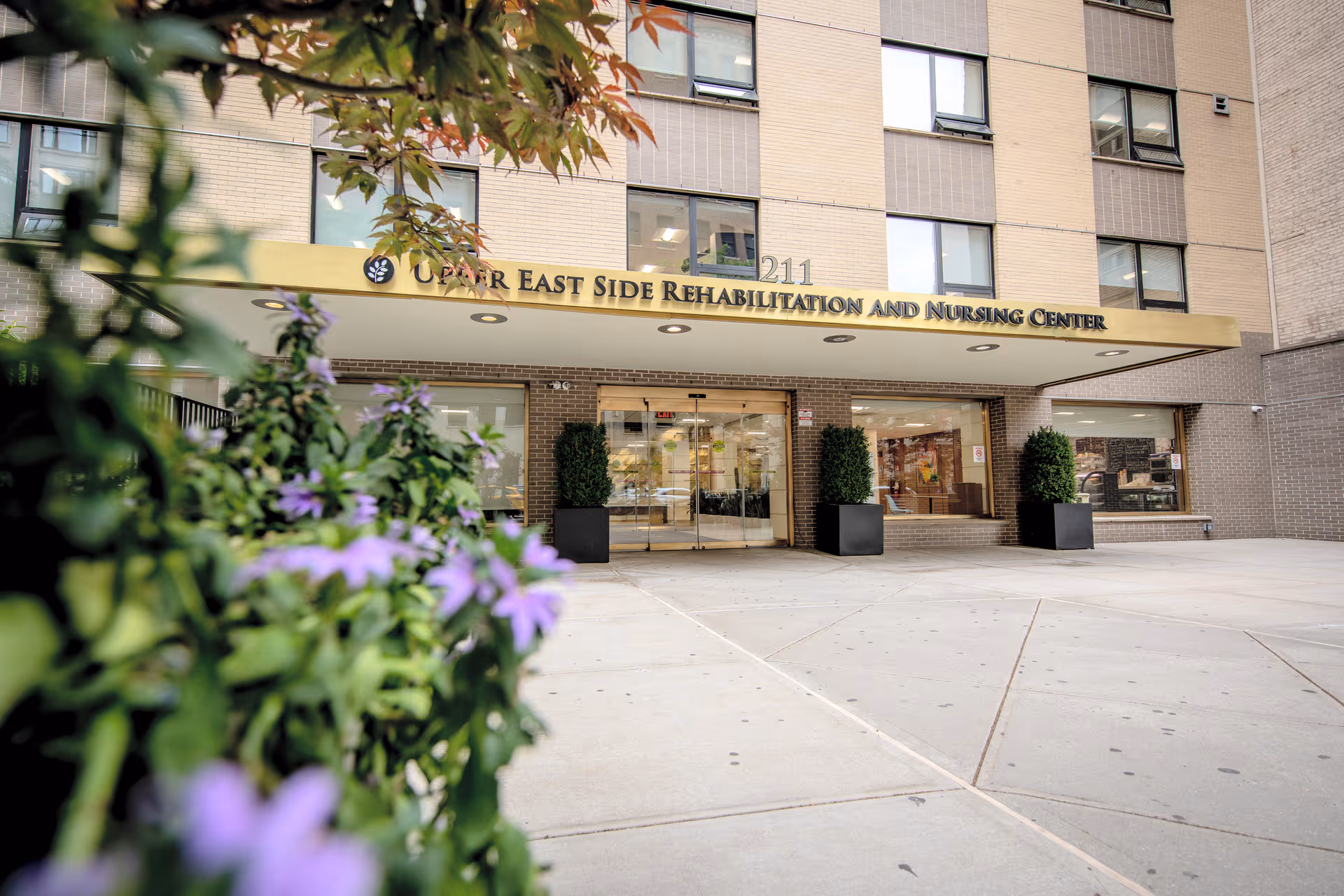 Front view of Upper East Side Rehabilitation and Nursing Center entrance with glass doors.