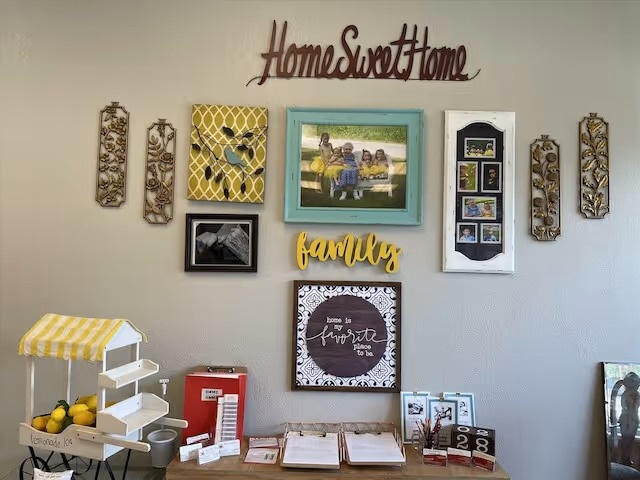 Wall display in senior living common area with photo frames and Home Sweet Home sign.