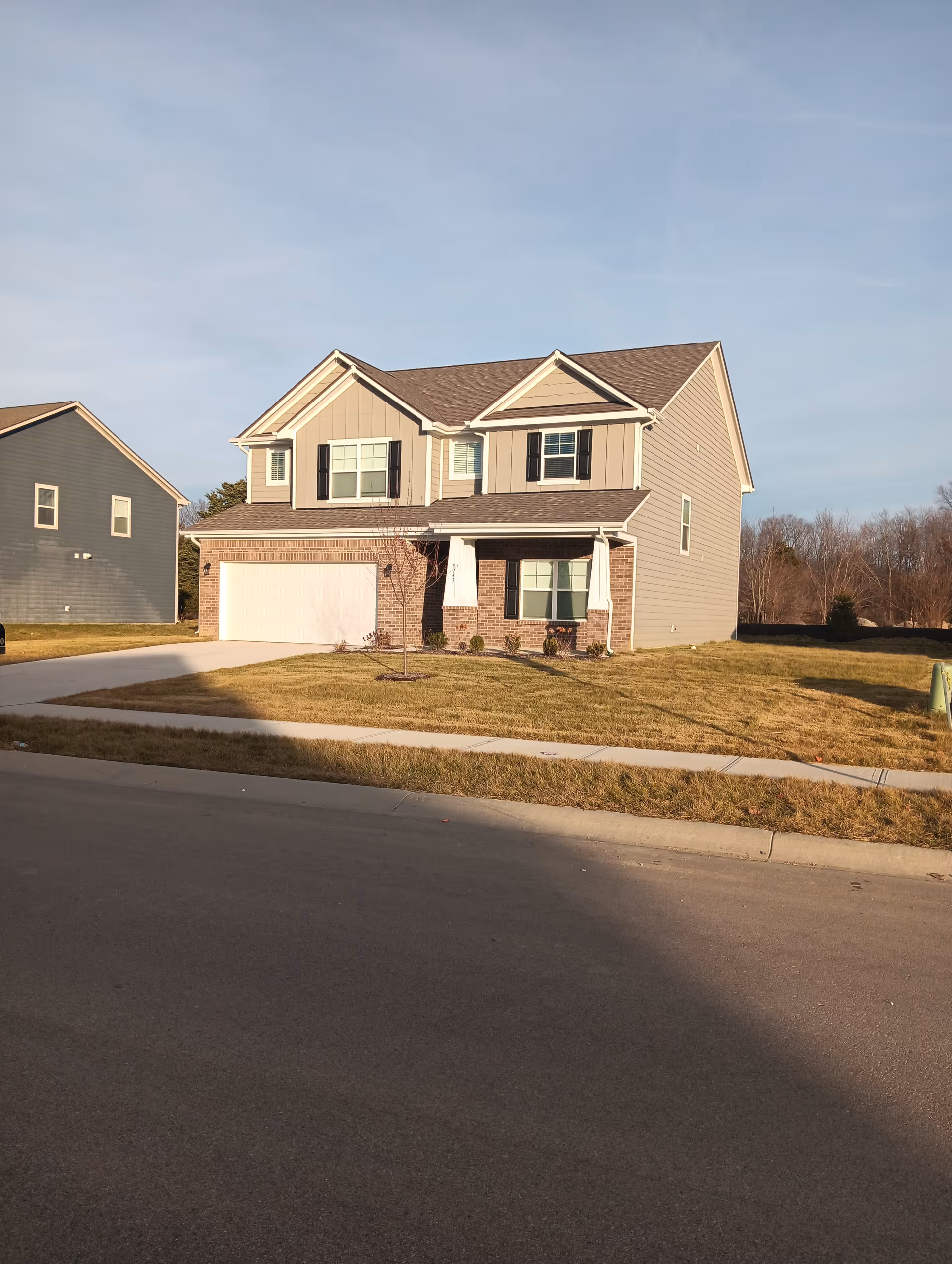 A two-story suburban house with a two-car garage, brick accents, and a grassy front yard.