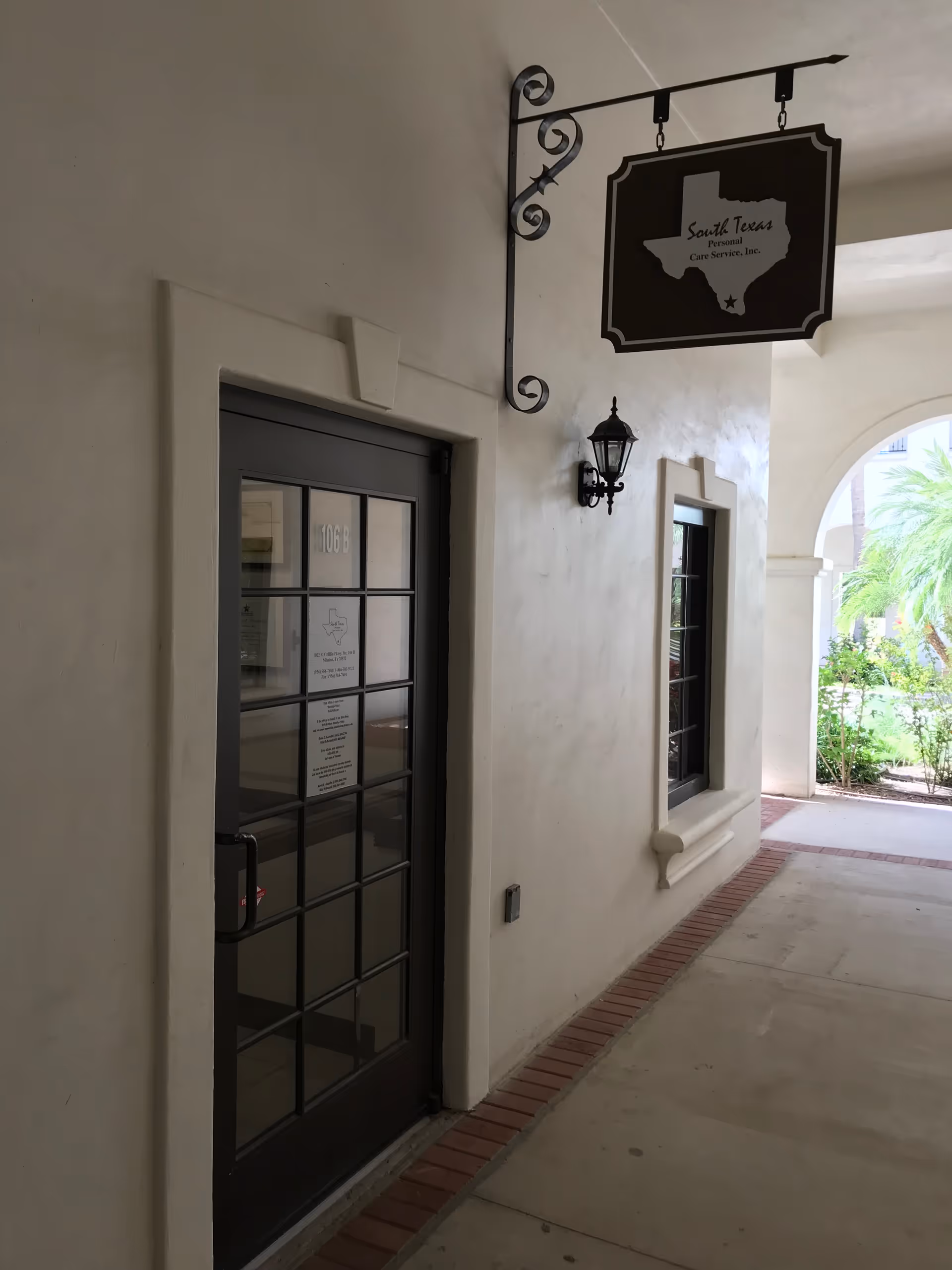 Exterior view of a facility entrance with a hanging sign and windowed door along walkway.
