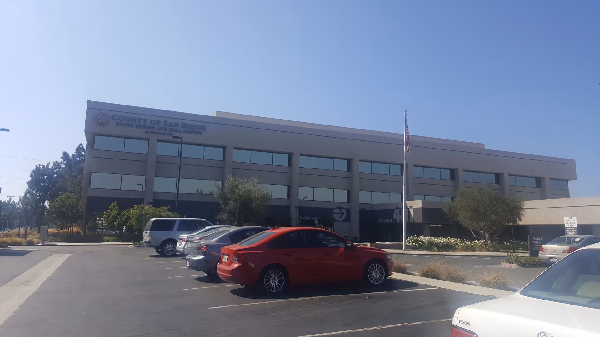 Exterior view of a multi-story office building with parked cars and a flagpole