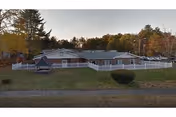 One-story facility with a white fence and autumn trees surrounding Apple Rehab Farmington Valley.
