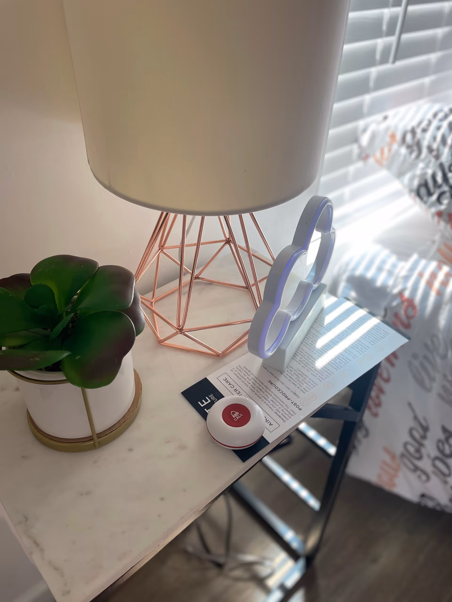 Marble bedside table with lamp, plant, and call button beside a bed