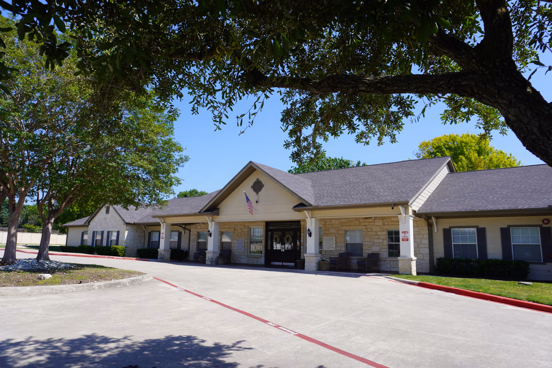 Senior living facility entrance with stone facade, covered walkway, and surrounding trees.