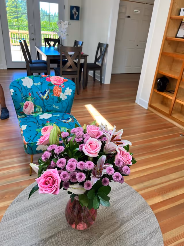 Sunlit interior with a colorful floral bouquet on a round table near a dining area.