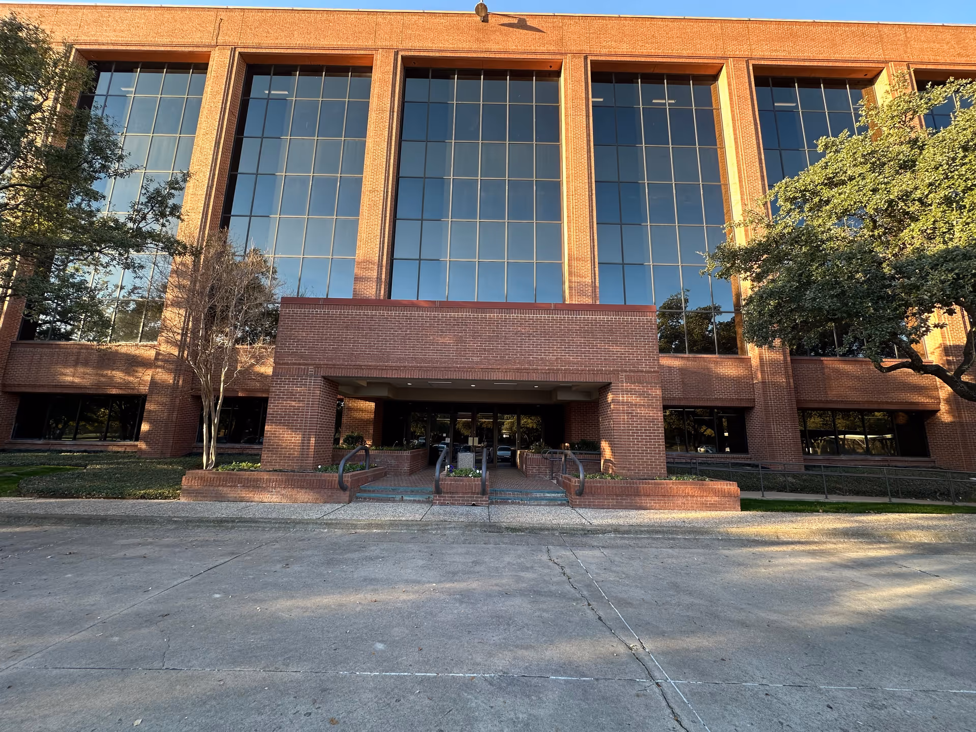 Brick building with tall glass windows and central entrance, flanked by trees.