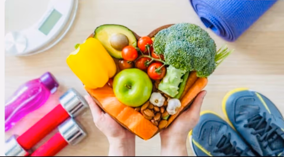 Hands hold a heart-shaped tray of fresh vegetables and fruit indoors.