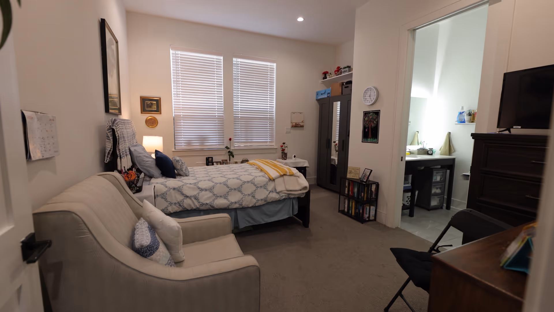 Cozy bedroom in a senior living facility with bed, sofa, desk, and adjacent bathroom.