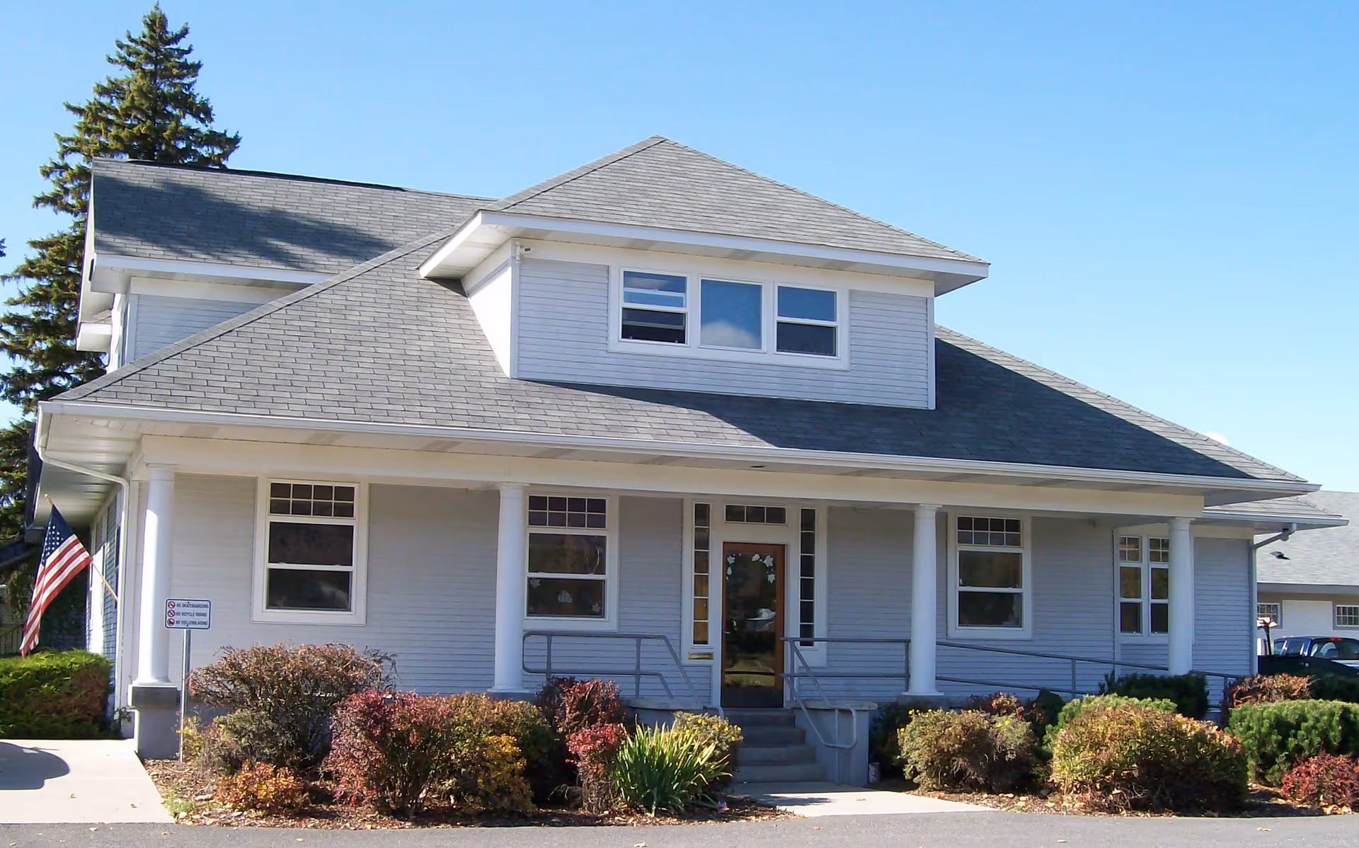 Front exterior of a white, two-story senior living facility with a porch and landscaping.