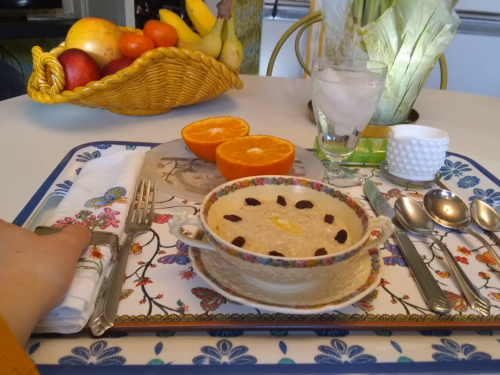 Indoor dining table with fruit basket, oatmeal bowl, glass, and cutlery.