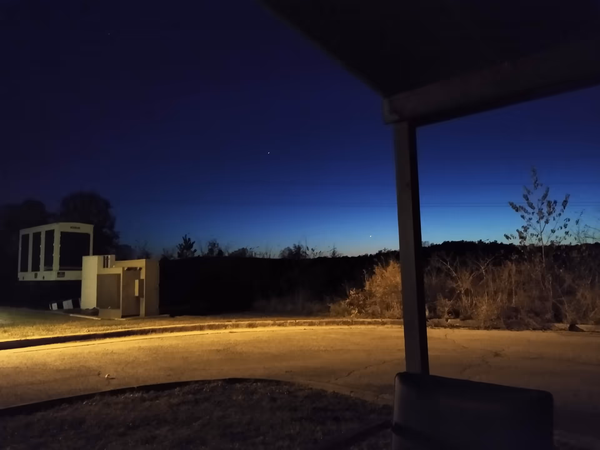 Night exterior of the facility showing an outdoor seating area and utility equipment.