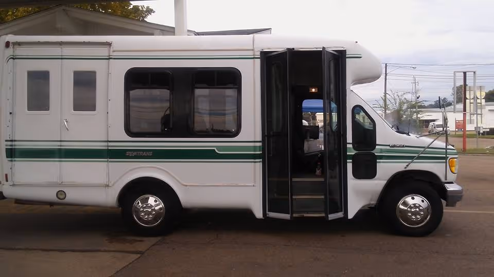 White shuttle bus with green stripes parked outdoors near a facility.