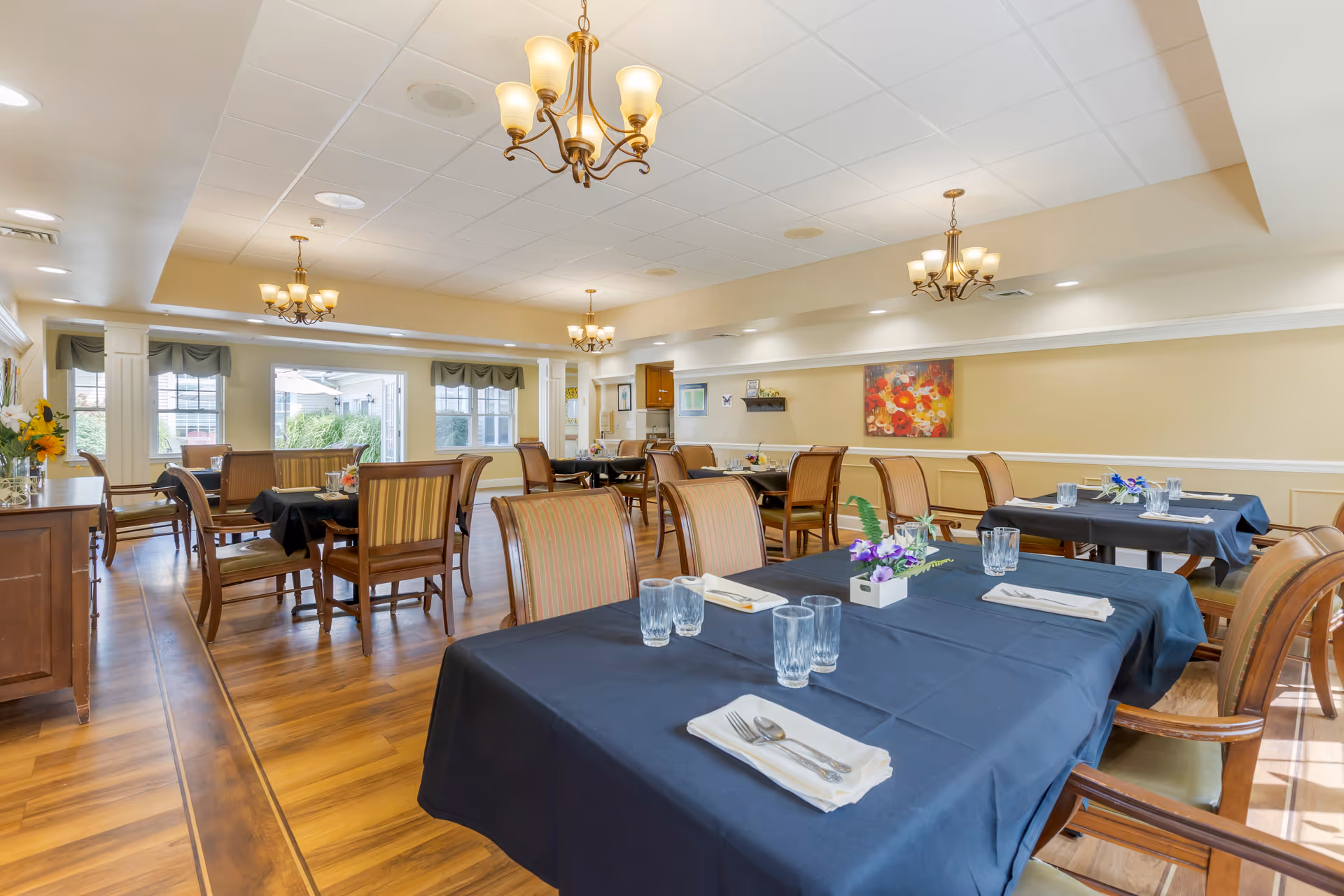 Bright dining hall with navy tablecloths, chairs, chandeliers, and floral centerpieces.