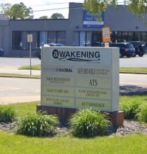 Outdoor sign in front of a building listing multiple tenants and landscaping.