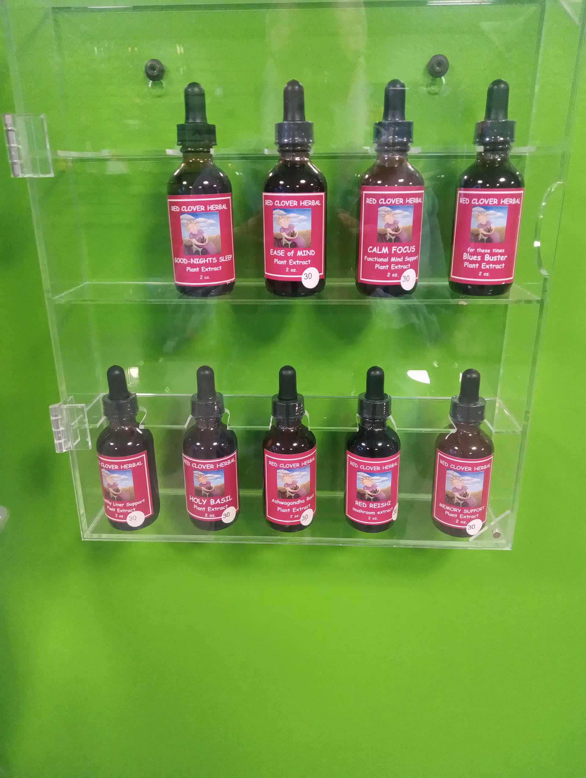 Rows of red clover herbal extract bottles on a clear shelf against a bright green wall.