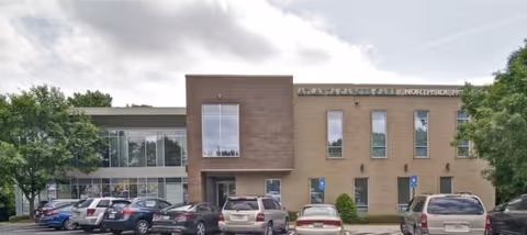 Exterior view of a brick medical building with glass windows and several parked cars.