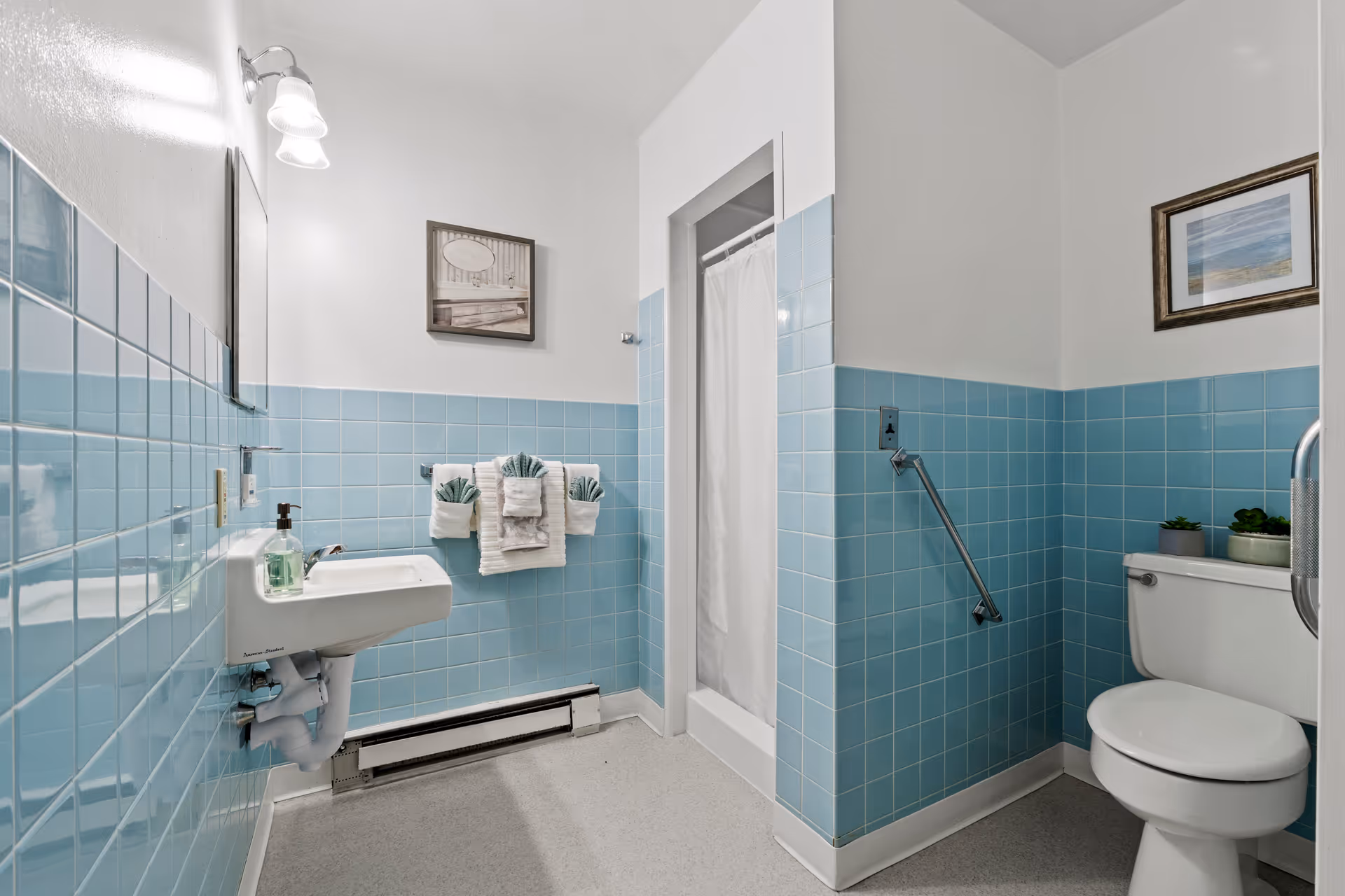 Blue-tiled bathroom with sink, toilet, shower curtain, towels in a senior living facility.