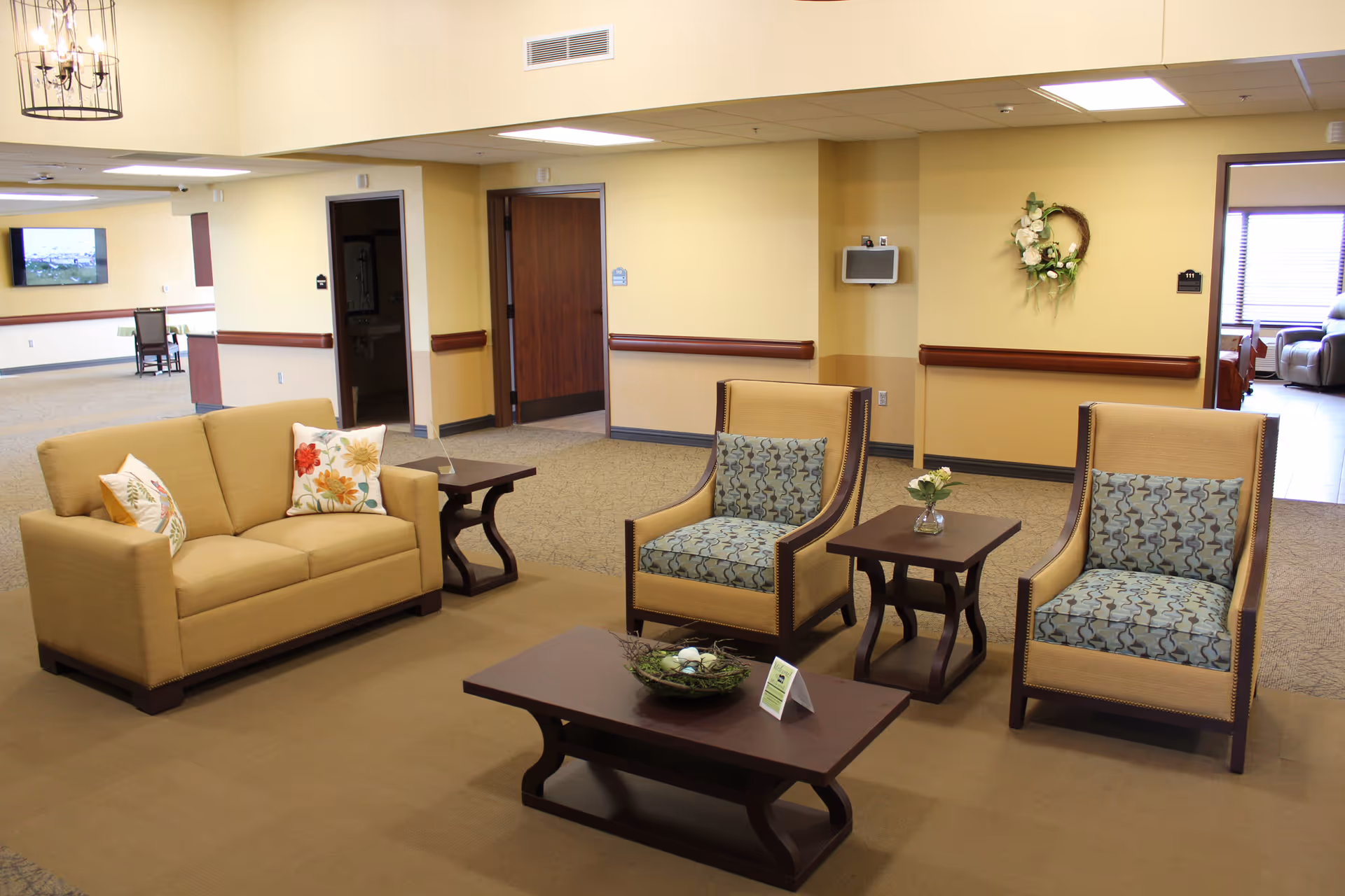 Spacious lobby with beige sofa, two patterned chairs, and coffee tables in a senior living facility.