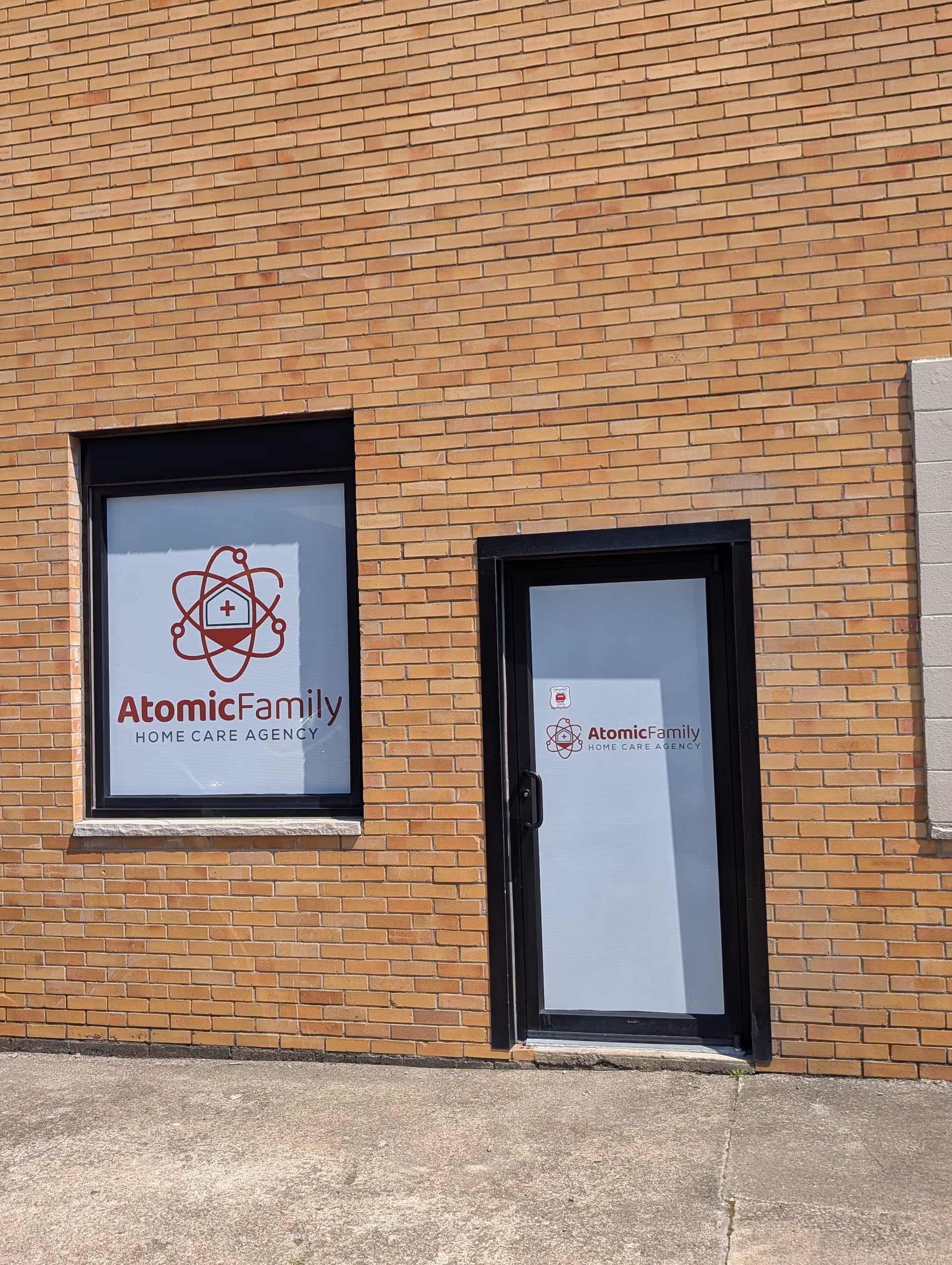 Exterior brick wall with a door and window displaying Atomic Family Home Care Agency.