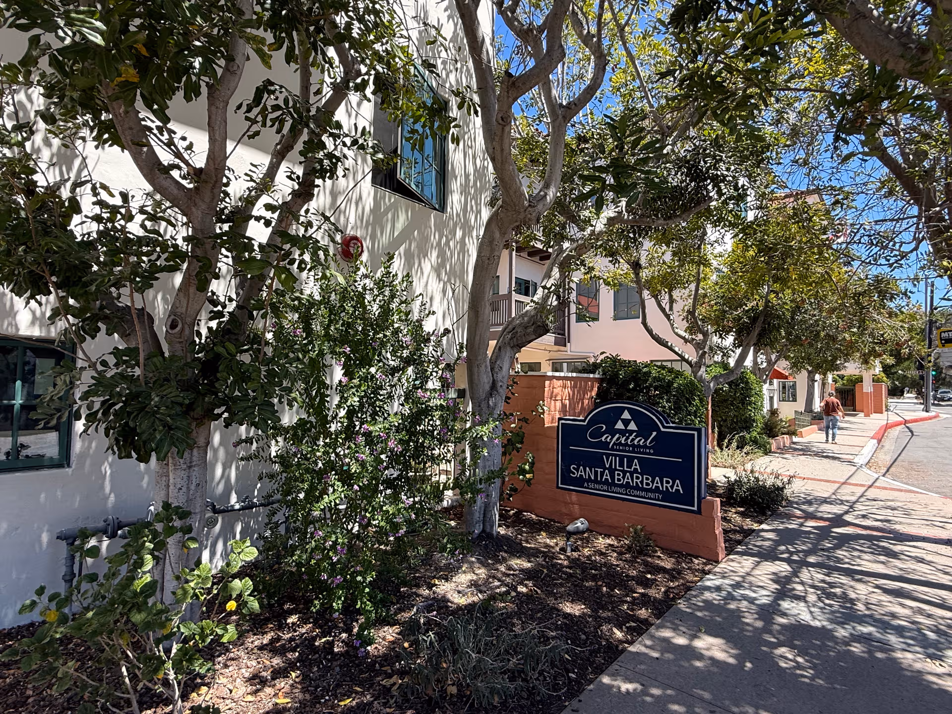Exterior view of Villa Santa Barbara building with a sign, trees, and a sidewalk.