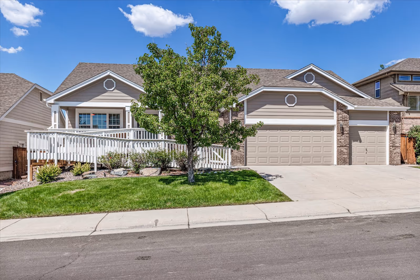 A beige, single-story building with white railing, green lawn, and a three-car garage.