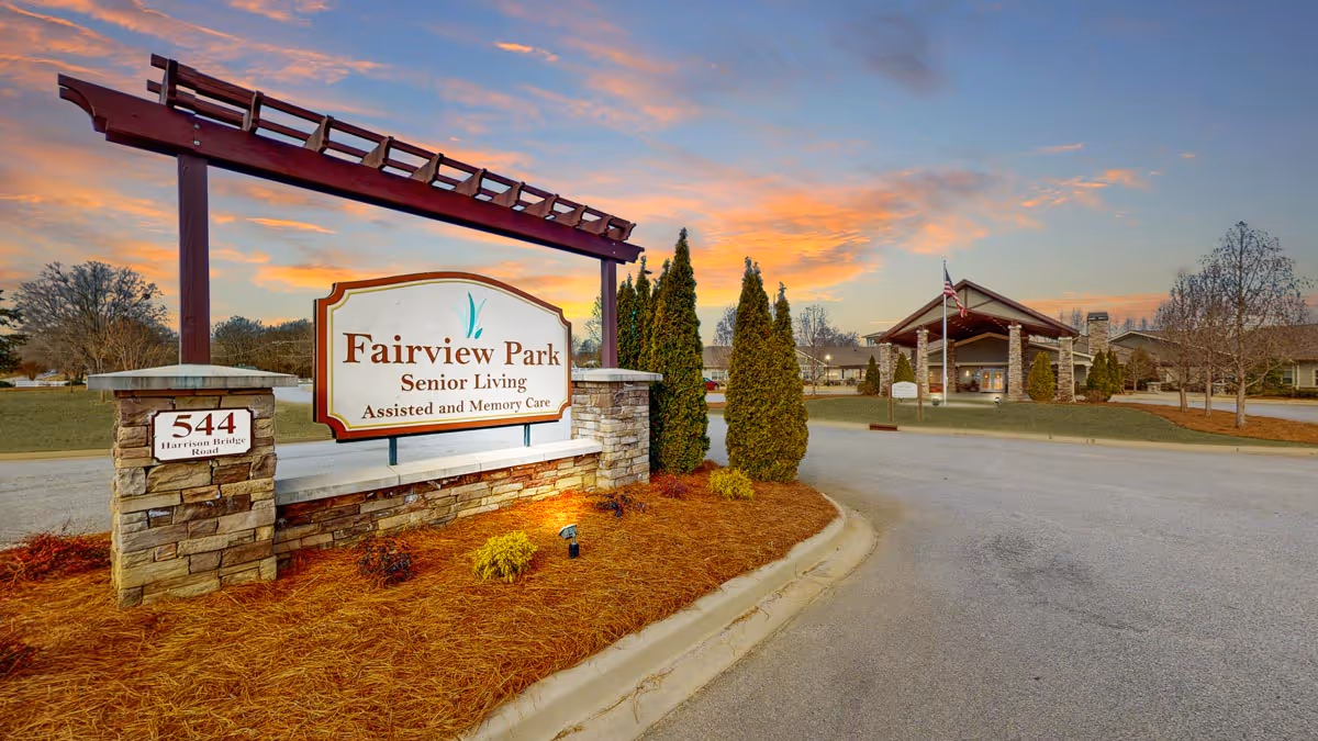 Entrance sign for Fairview Park Senior Living, Assisted and Memory Care, located at 544 Harrison Bridge Road, with the facility building and driveway visible in the background during sunset.