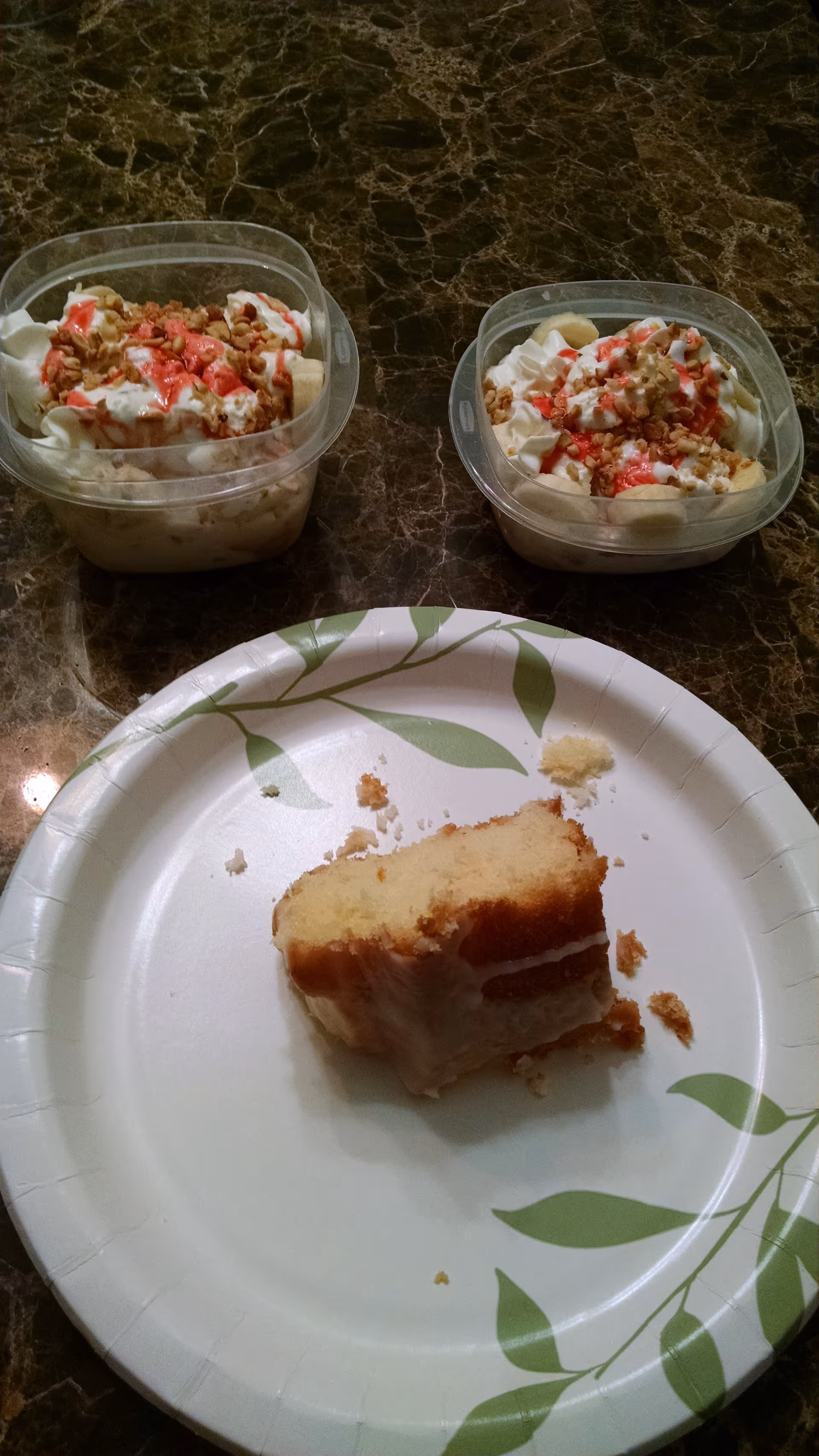Two yogurt cups with fruit and whipped cream beside a cake slice on a marbled counter.