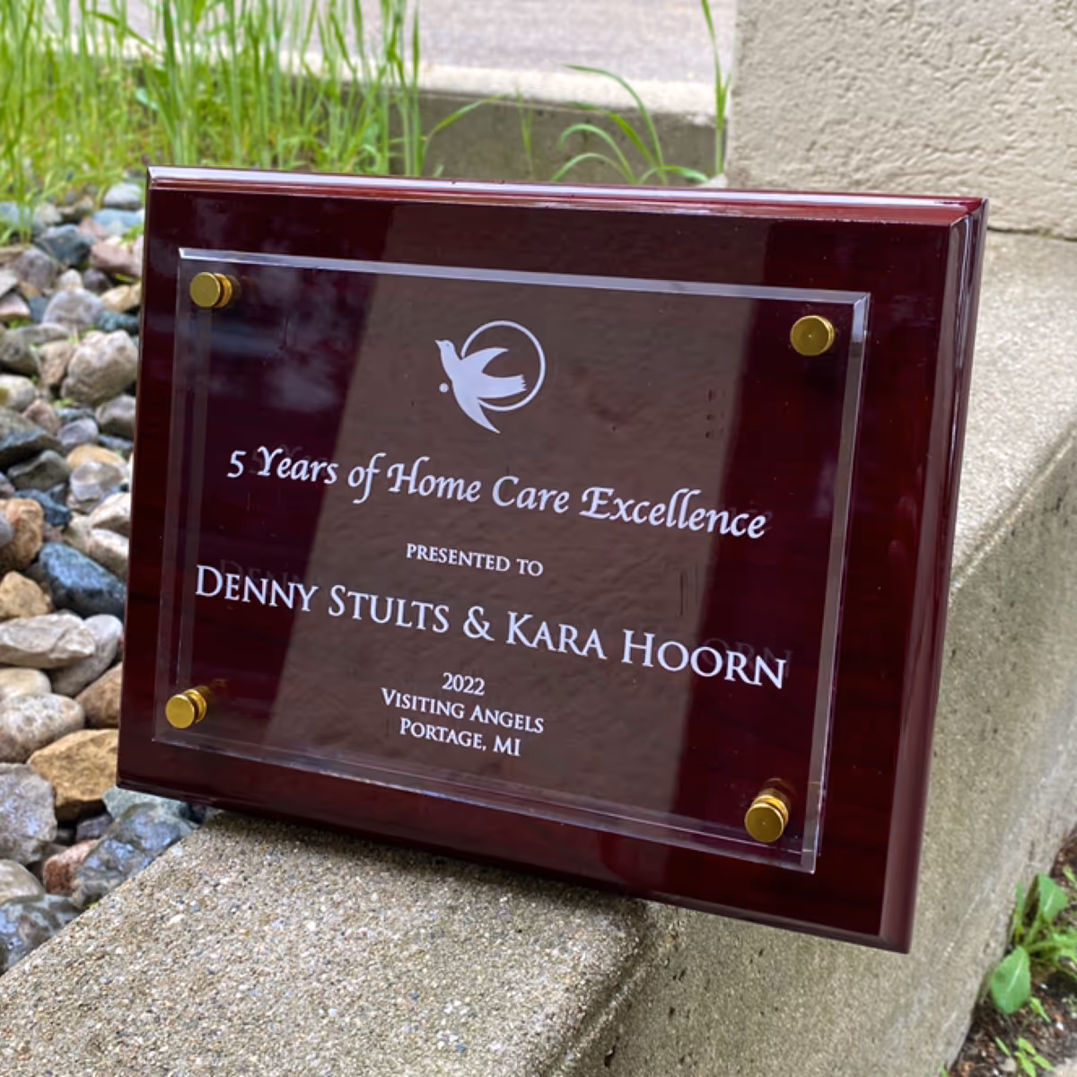 Close-up of a burgundy award plaque mounted outdoors with recipient names