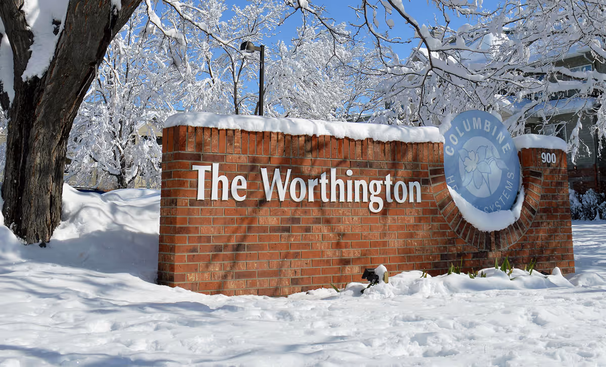 Snow covers a brick entrance sign reading The Worthington with a circular logo.