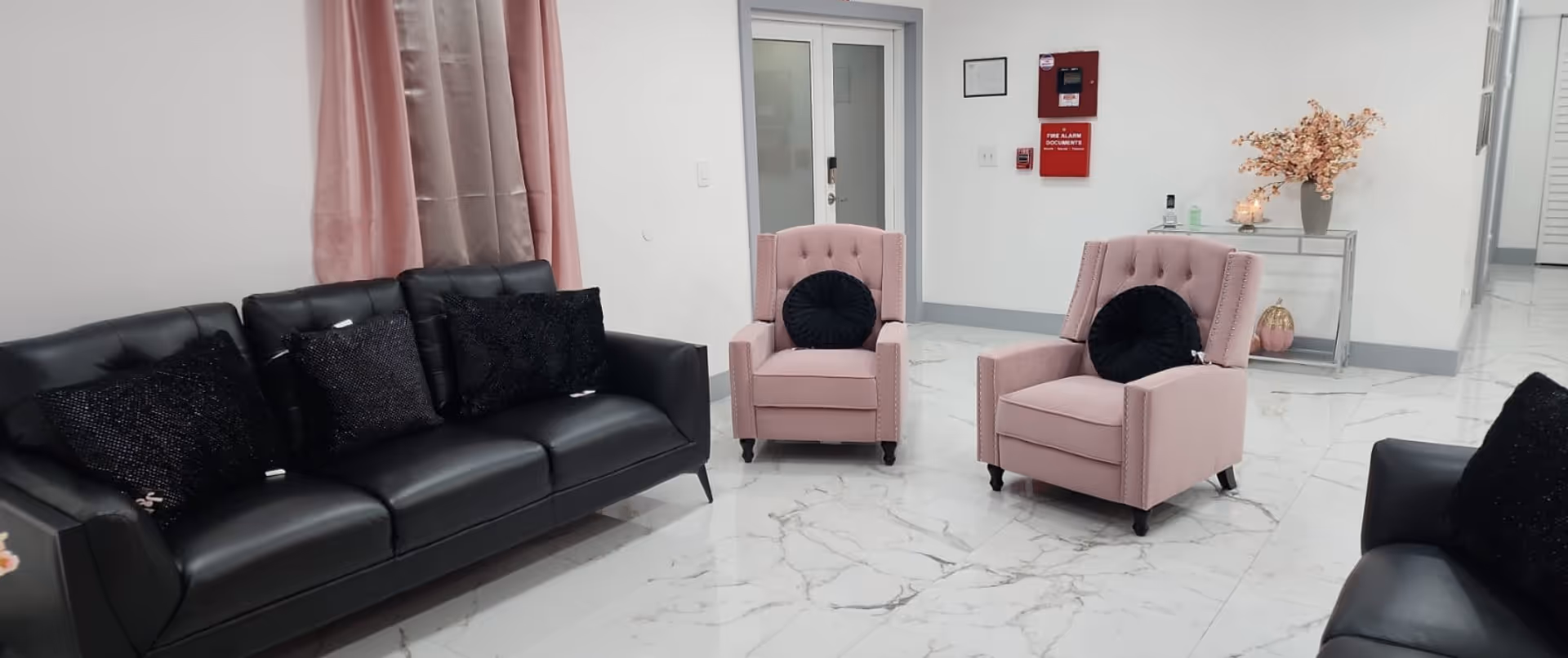 A modern living room with a black sofa and two pink armchairs.