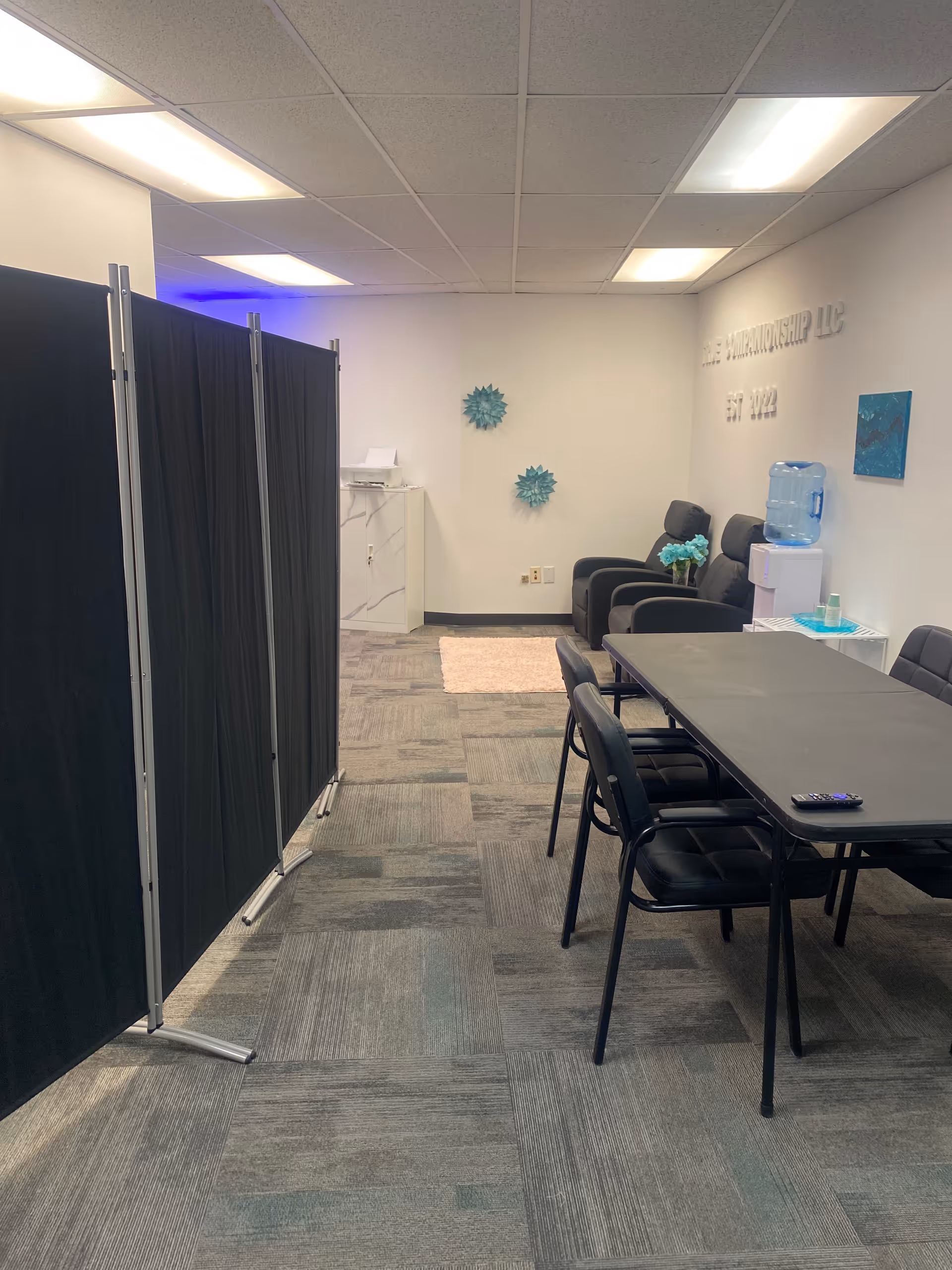 Interior meeting room with black folding partitions, a long table, chairs, and a water cooler.