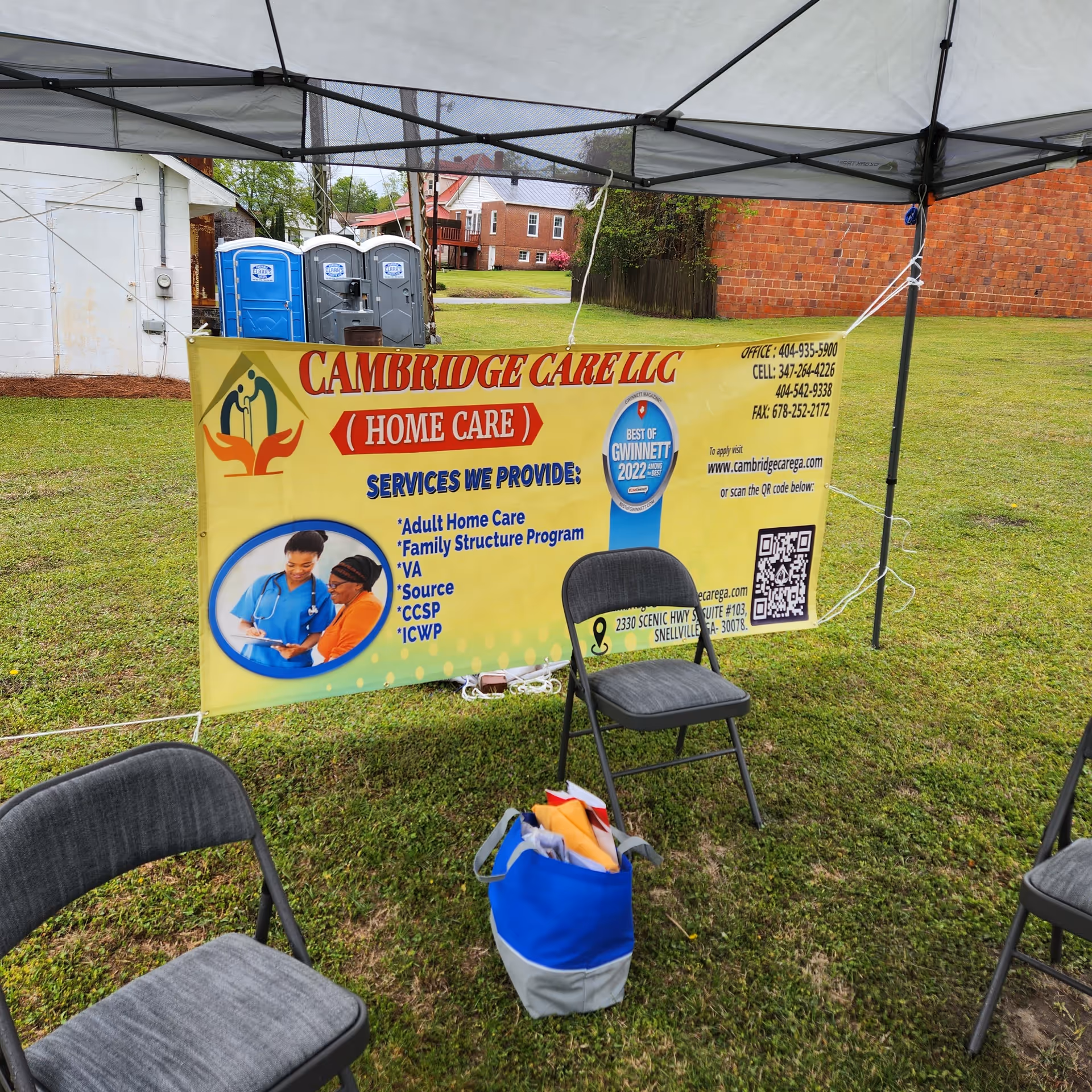 Outdoor event setup with Cambridge Care LLC banner under a canopy on grass.
