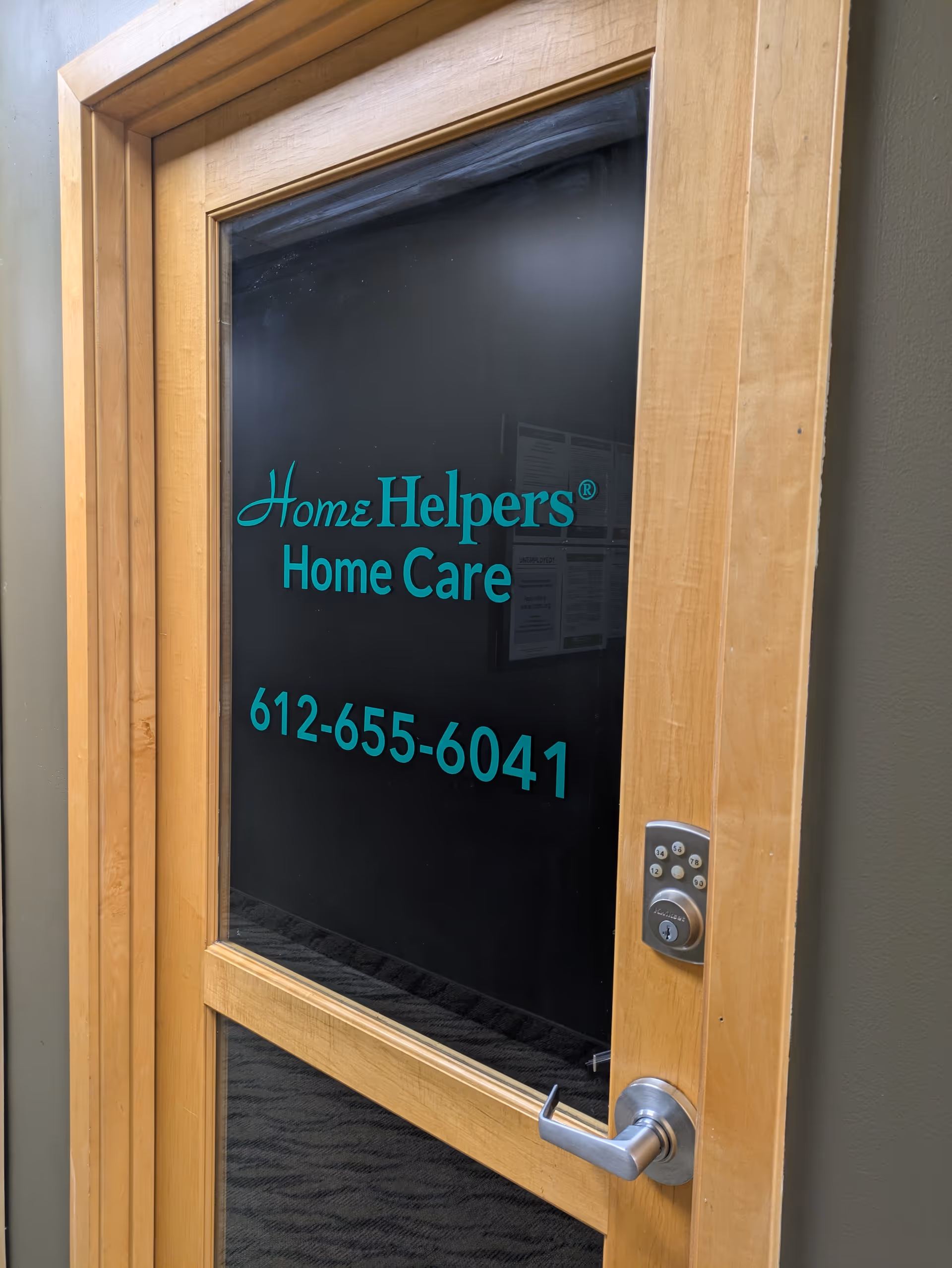 Wood-framed glass door with teal Home Helpers Home Care text and phone.