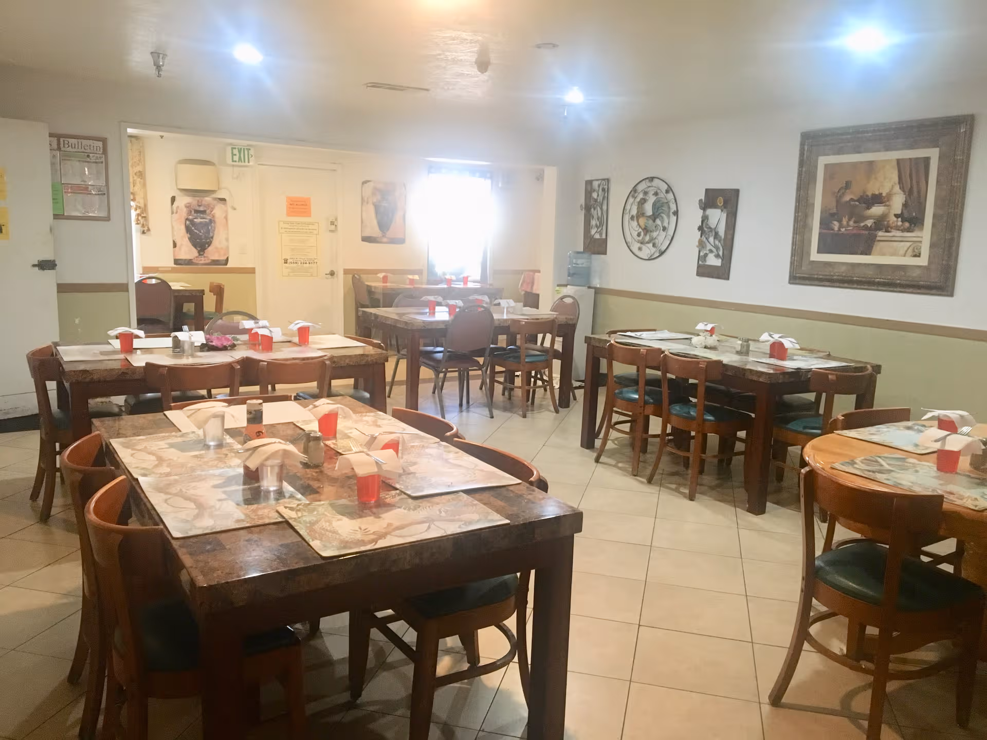 Well-lit senior dining room with several tables, chairs, and place settings.