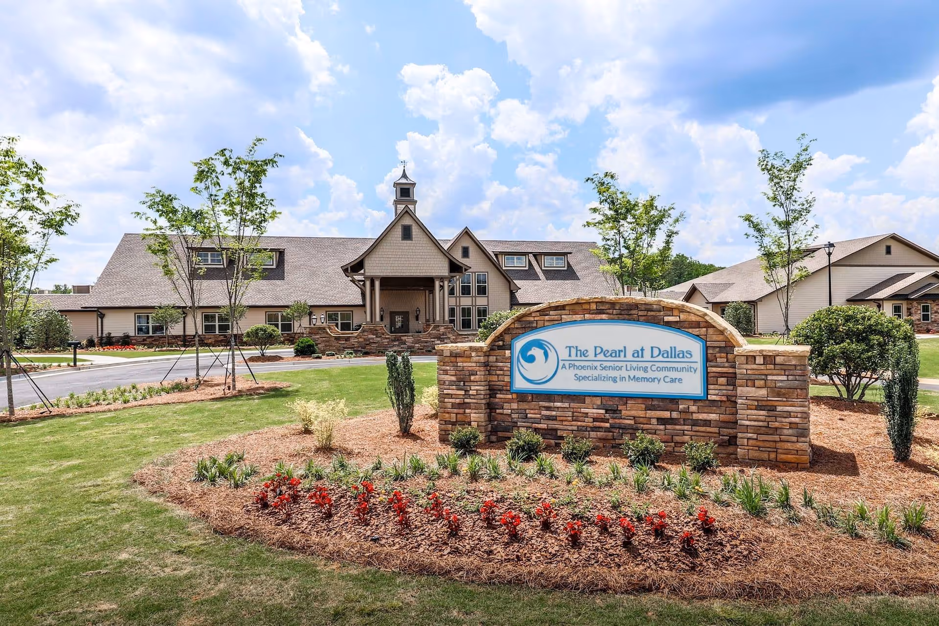 Exterior view of a senior living campus with a stone entrance sign and landscaping.
