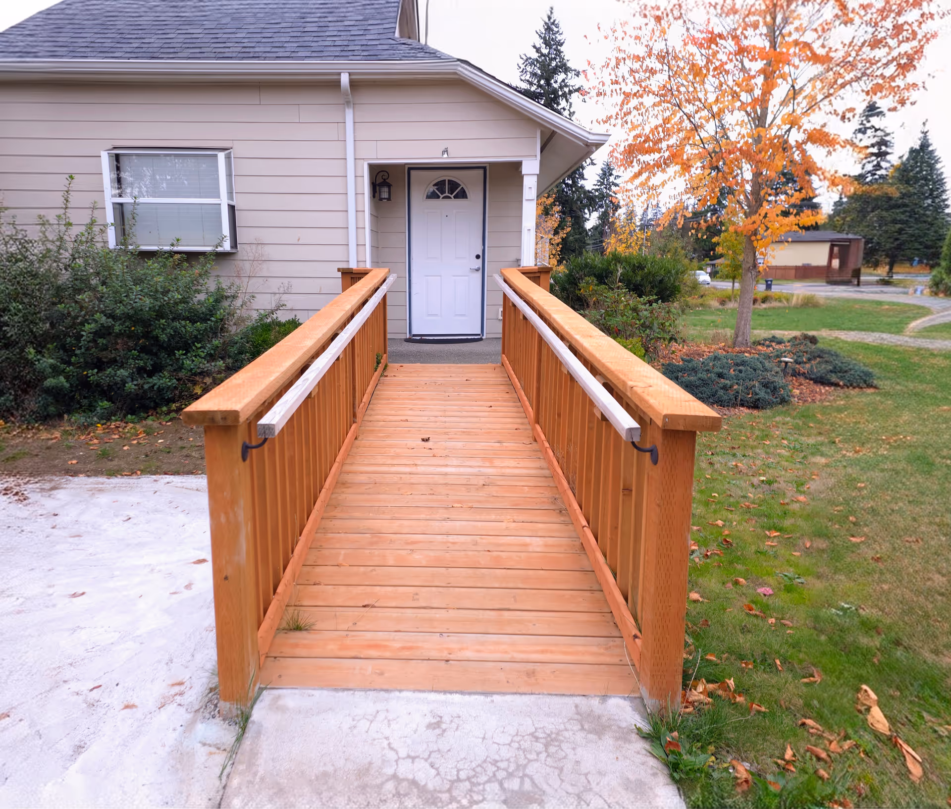 Wooden ramp leads to a beige building entrance with autumn trees.