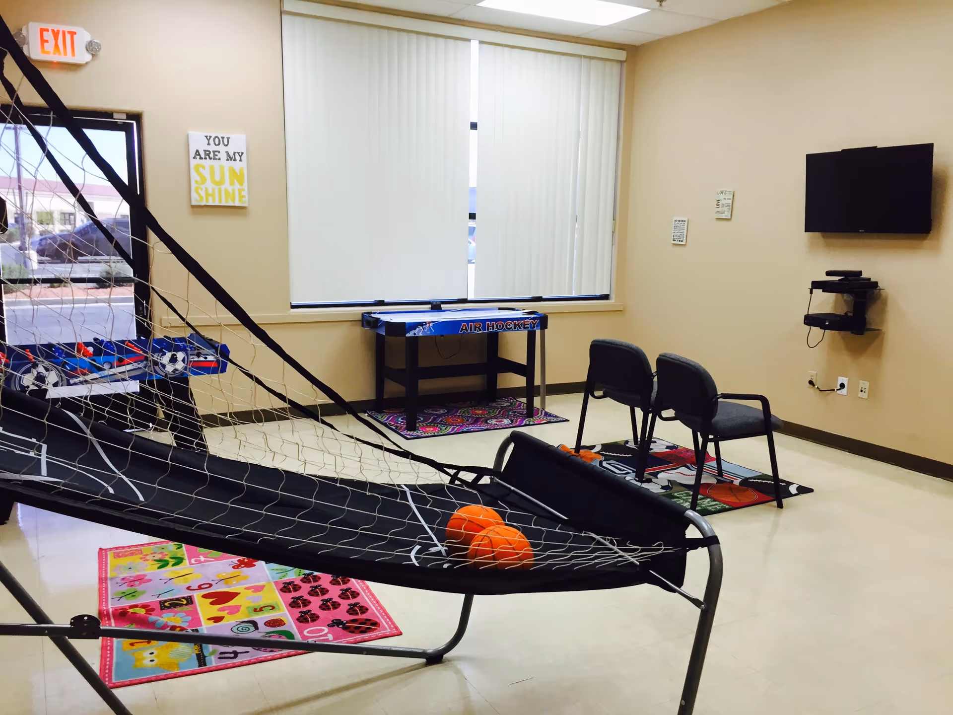 Recreation room with air hockey table, hammock, chairs, TV, and colorful mats.