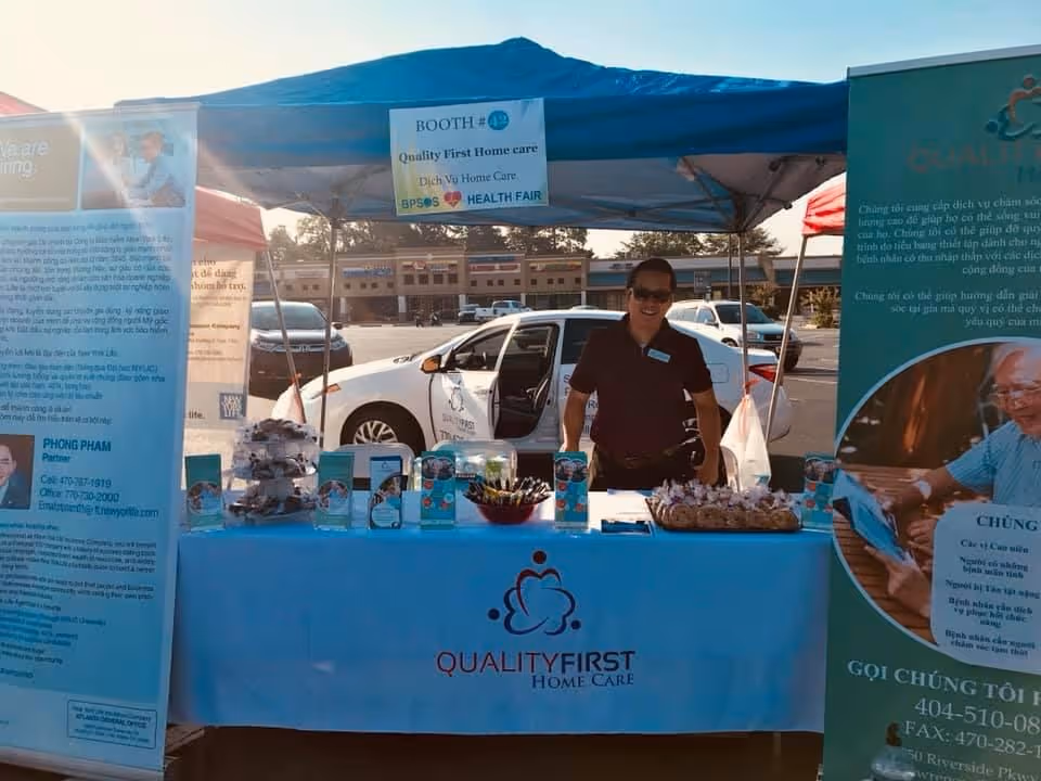 A man stands behind a blue table at an outdoor booth for Quality First Home Care.