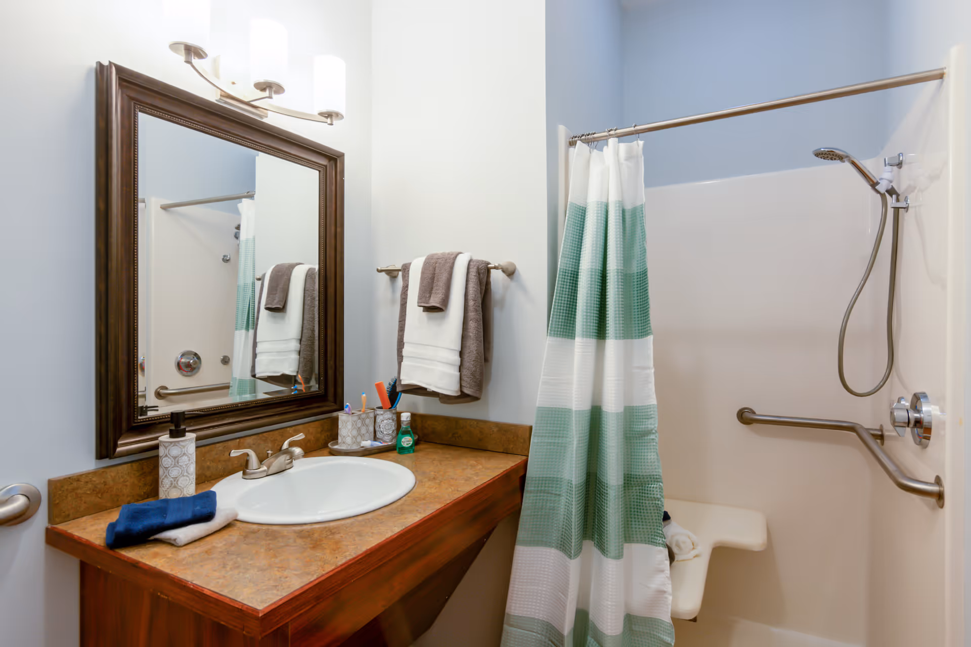 Bathroom vanity with sink, mirror, towels, and striped shower curtain in a senior living unit.