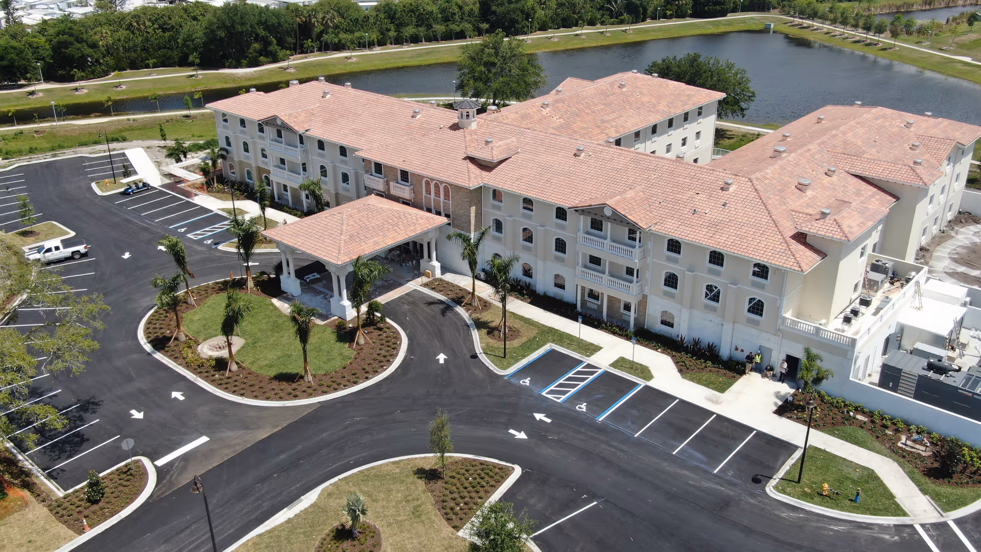 A large beige senior living building with red tile roof, circular drive, and surrounding parking.