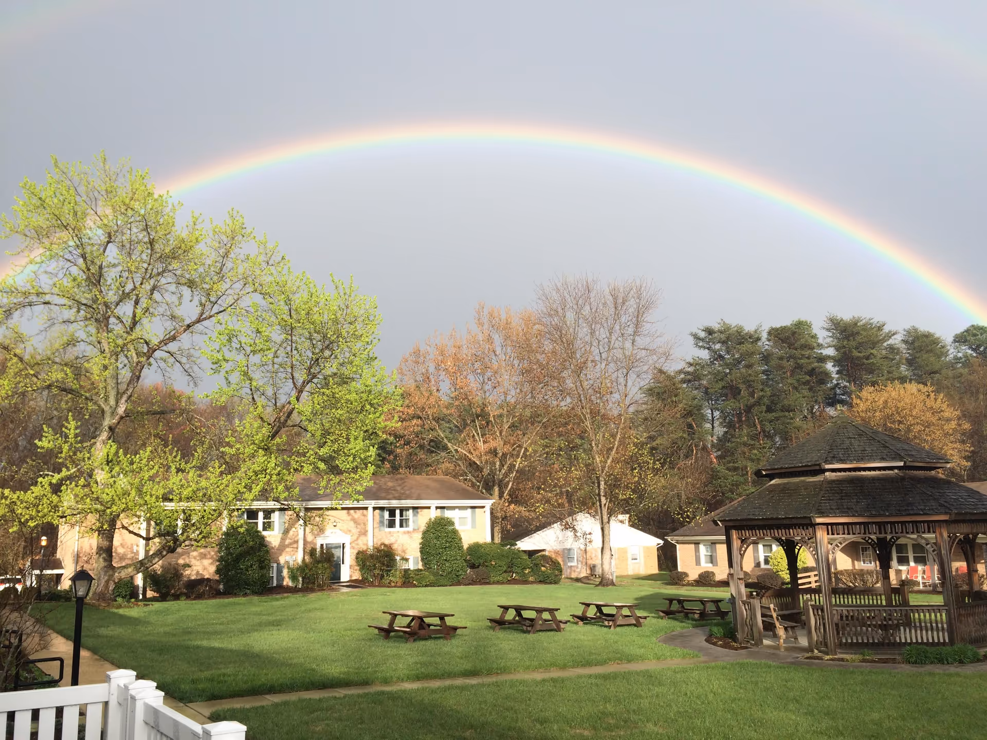 Rainbow arches over a sunny outdoor courtyard with picnic tables and a gazebo.