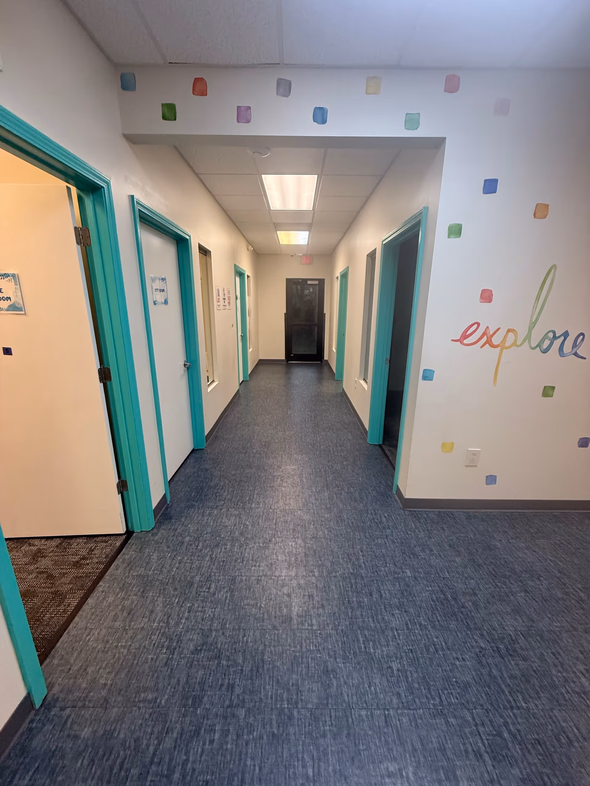 Long hallway with teal door frames and colorful wall squares in a care facility