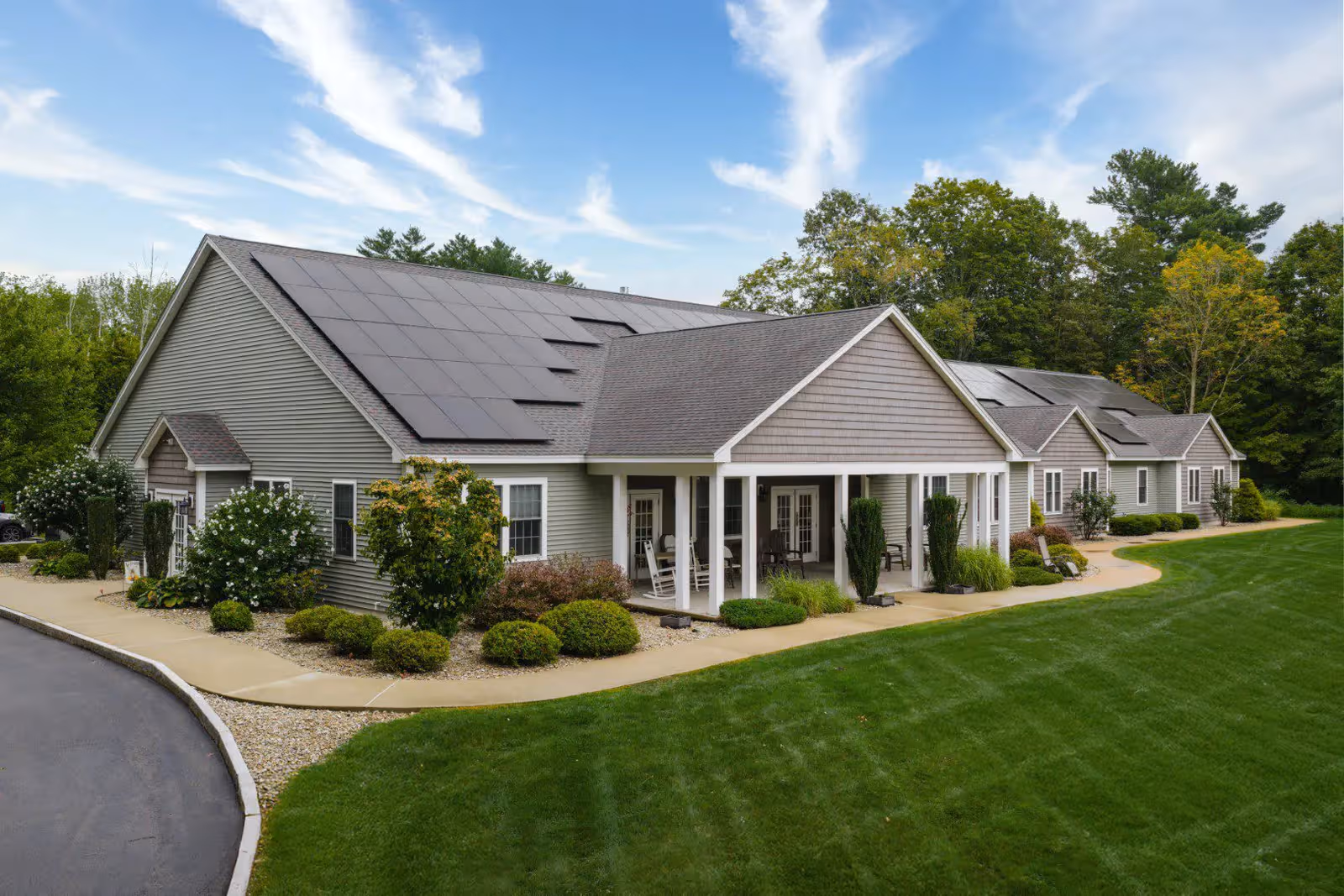 A single-story assisted living campus with gray siding, peaked roofs, and a landscaped front yard.