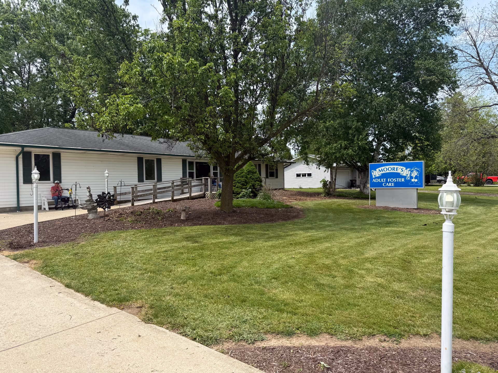 Single-story facility exterior with Moore's Adult Foster Care sign, trees, and a surrounding lawn.