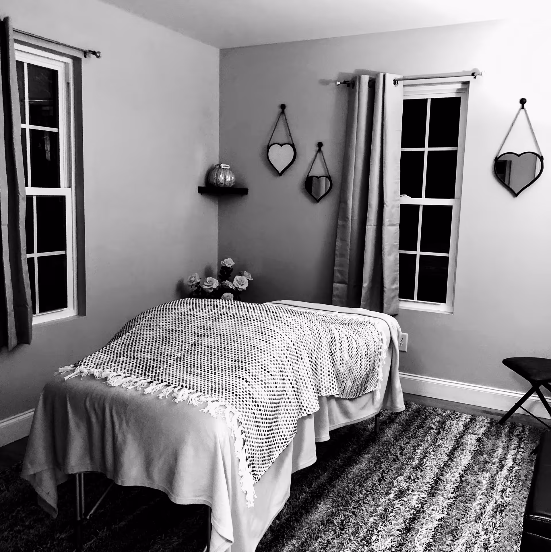 Cozy bedroom in a senior facility featuring a bed, windows, heart mirrors, curtains, and flowers.