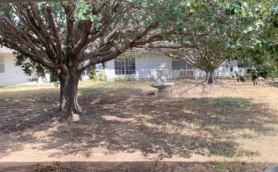 Wide view of Greystone Park exterior with large trees, lawn, and a stone fountain.