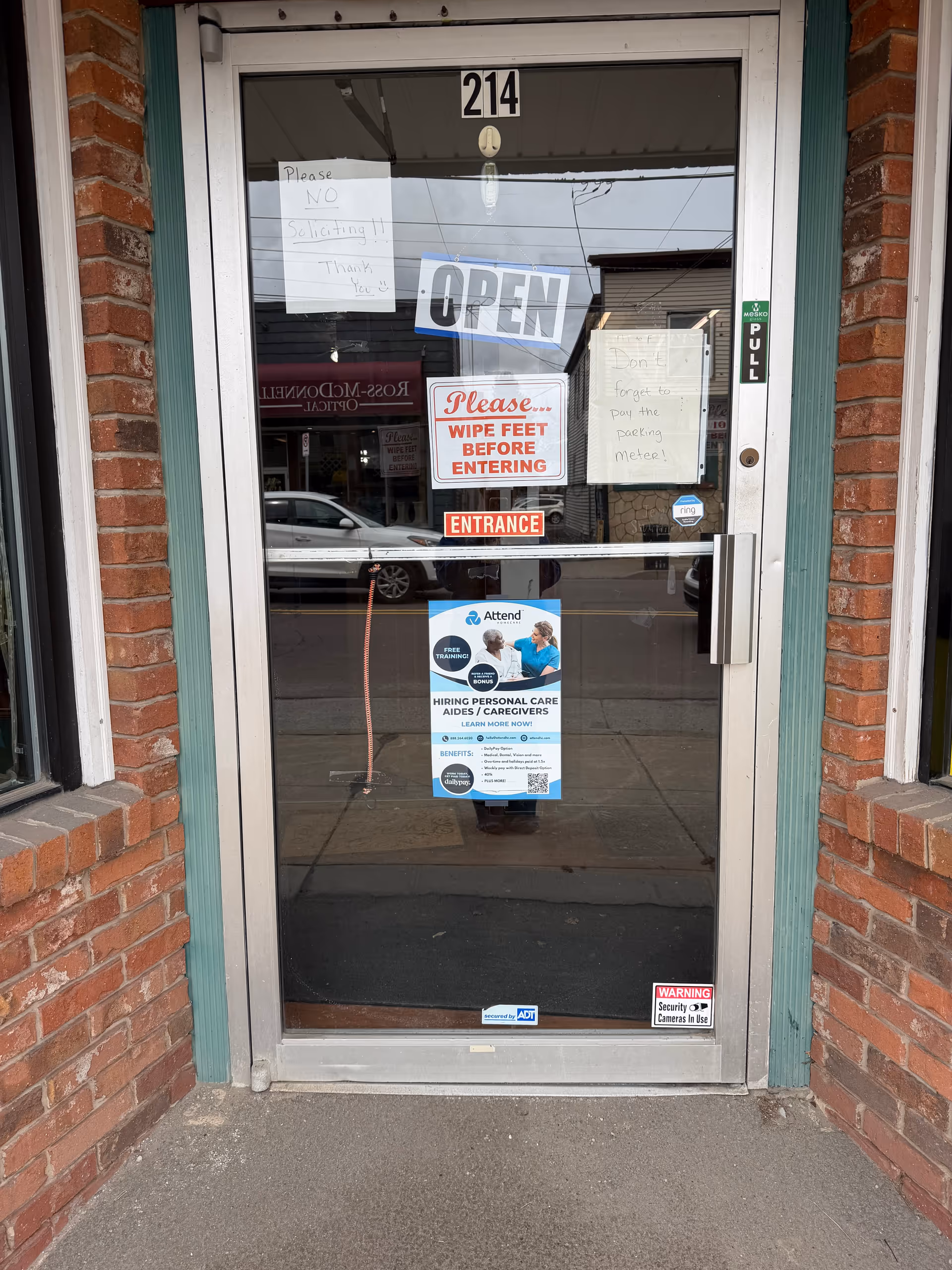 Brick-front entrance with glass door, open sign, and posted notices.