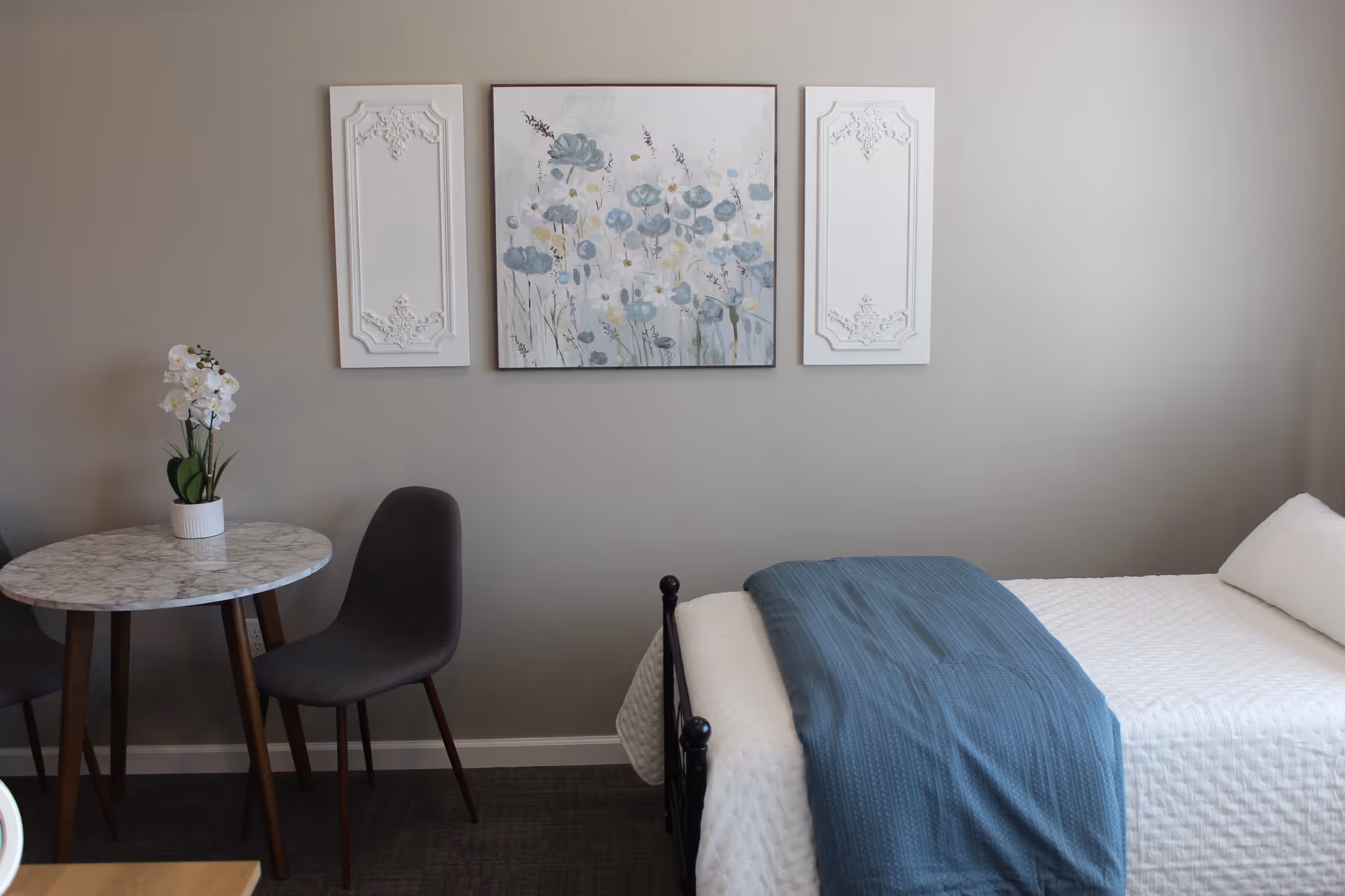 Cozy bedroom in a senior living facility with bed, round marble table, chairs, and wall art.