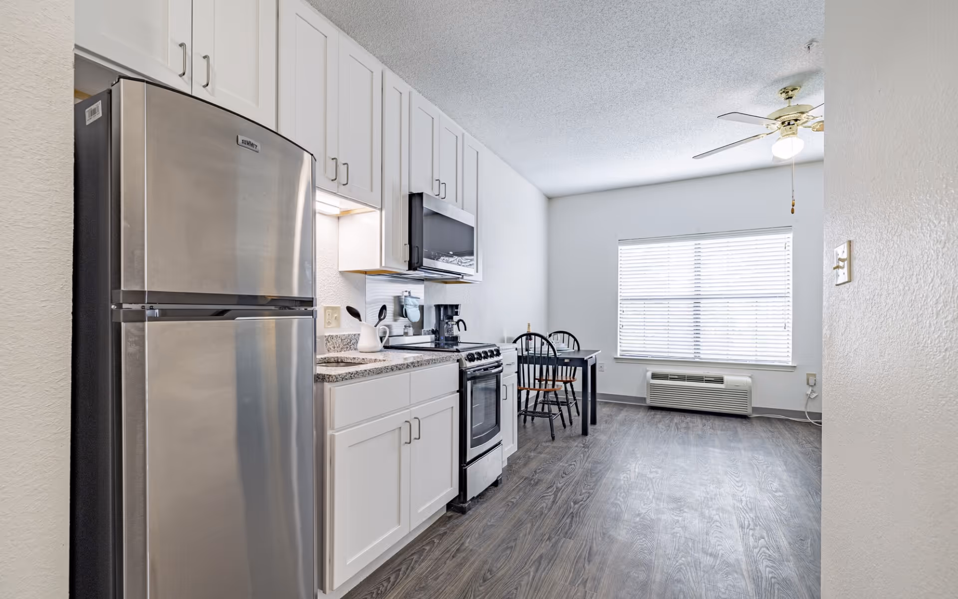 Modern kitchen with stainless steel refrigerator, stove, microwave, white cabinets, and small dining table.