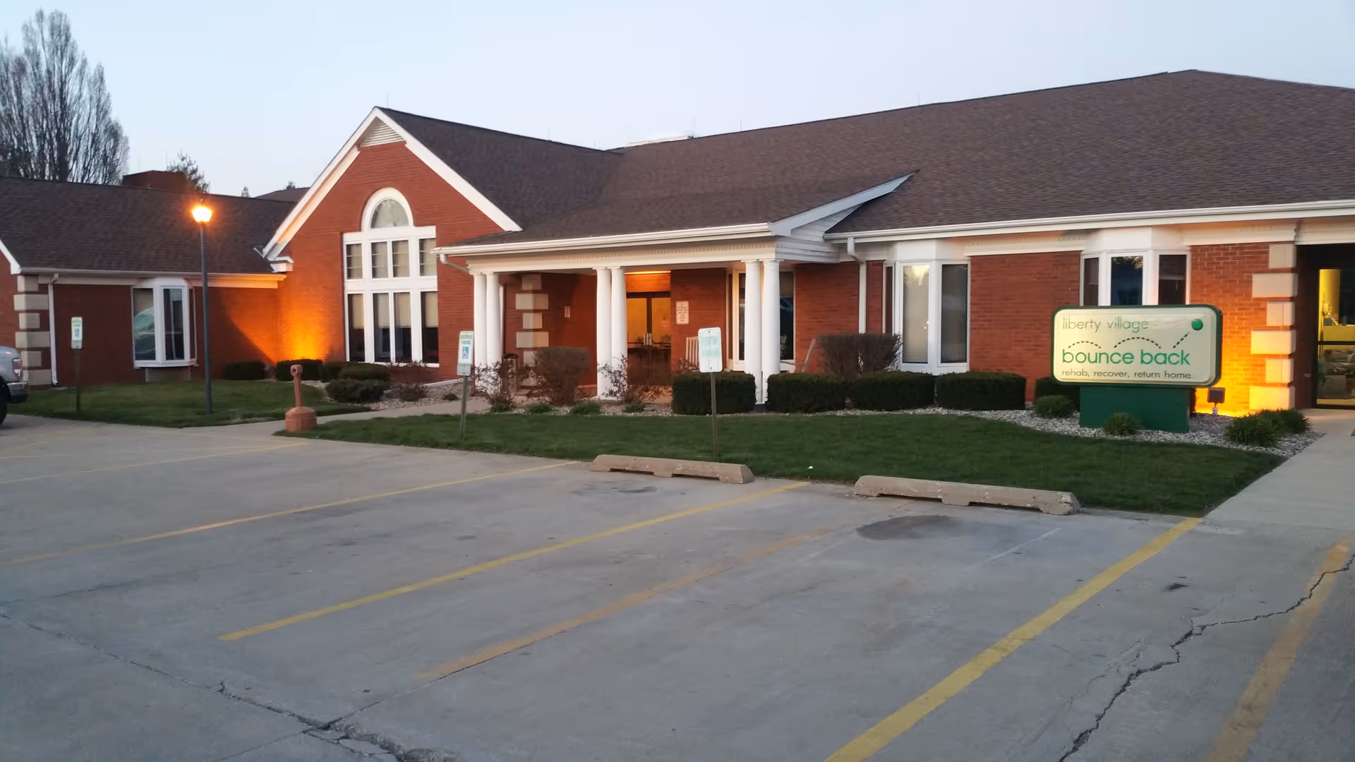 Single-story brick senior living facility with a driveway, parking lot, and entrance with columns.